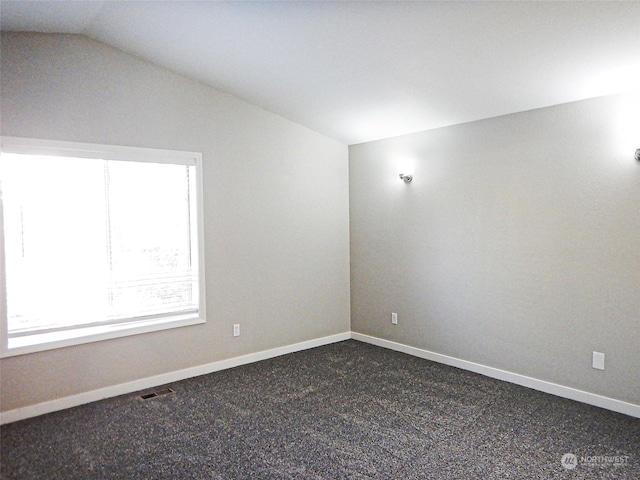 unfurnished room featuring dark colored carpet, visible vents, vaulted ceiling, and baseboards