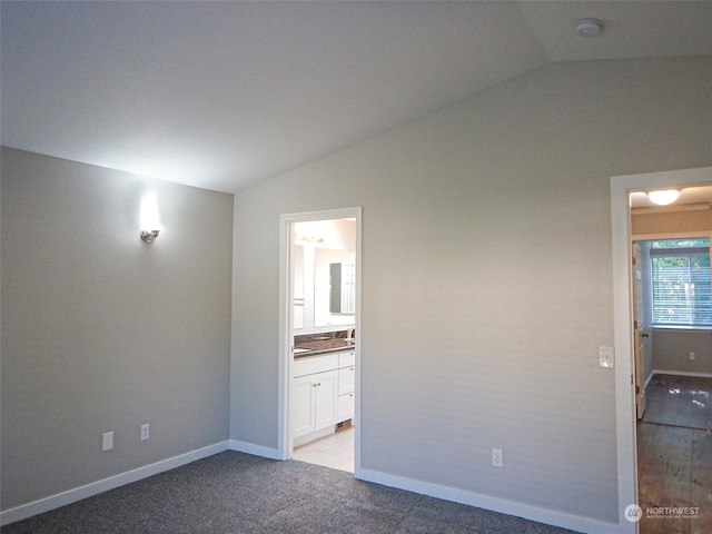 unfurnished bedroom with lofted ceiling, light colored carpet, connected bathroom, and baseboards