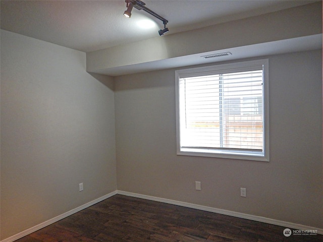 spare room with dark wood-style floors, baseboards, visible vents, and track lighting