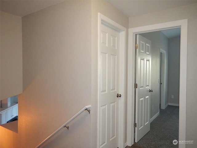 hallway featuring baseboards, dark colored carpet, and an upstairs landing