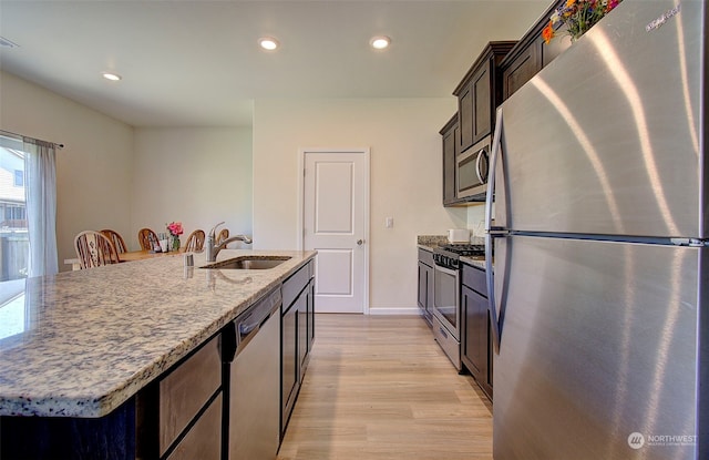 kitchen featuring light wood-type flooring, a kitchen island with sink, light stone counters, sink, and appliances with stainless steel finishes