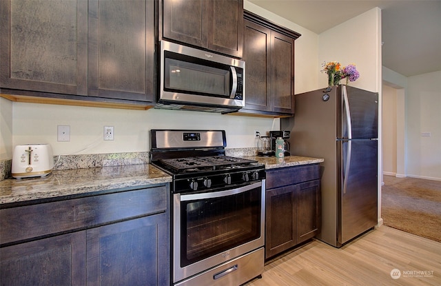 kitchen featuring dark brown cabinets, light stone counters, stainless steel appliances, and light colored carpet