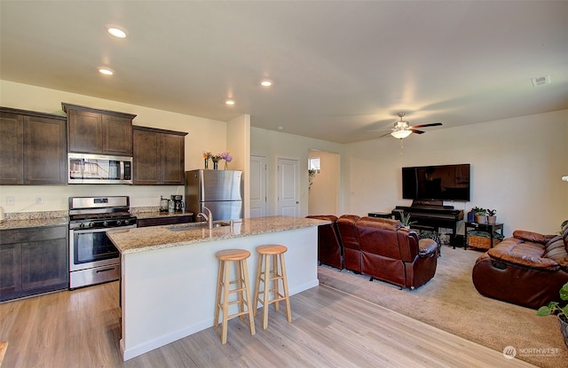 kitchen featuring appliances with stainless steel finishes, light hardwood / wood-style floors, an island with sink, sink, and ceiling fan