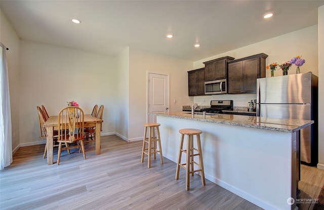 kitchen with light wood-type flooring, appliances with stainless steel finishes, light stone countertops, and a center island with sink