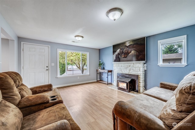 living room featuring a stone fireplace, plenty of natural light, and light hardwood / wood-style floors