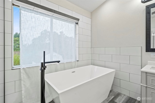 bathroom with wood-type flooring, a tub to relax in, vanity, and tile walls