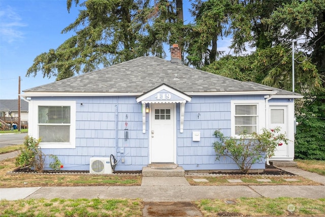 bungalow with roof with shingles, a chimney, and ac unit