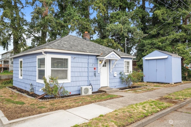 bungalow-style house with a chimney, roof with shingles, an outdoor structure, ac unit, and a shed