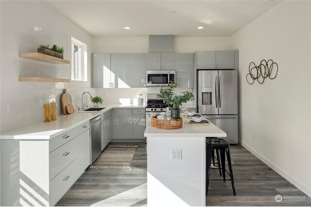 kitchen with sink, hardwood / wood-style flooring, appliances with stainless steel finishes, a center island, and a breakfast bar area