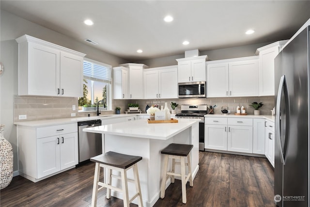 kitchen with dark hardwood / wood-style flooring, stainless steel appliances, white cabinetry, and a center island