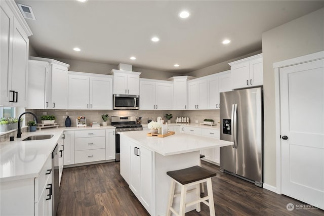 kitchen featuring stainless steel appliances, dark wood-type flooring, a kitchen island, sink, and white cabinetry