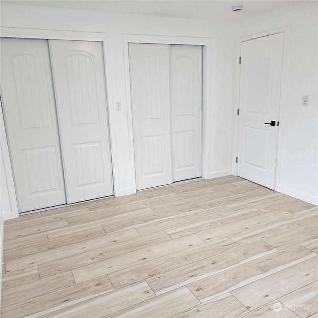 unfurnished bedroom with two closets and light hardwood / wood-style floors