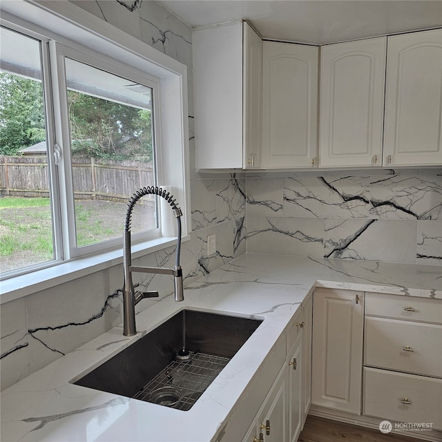 kitchen featuring white cabinetry, a wealth of natural light, light stone counters, and sink