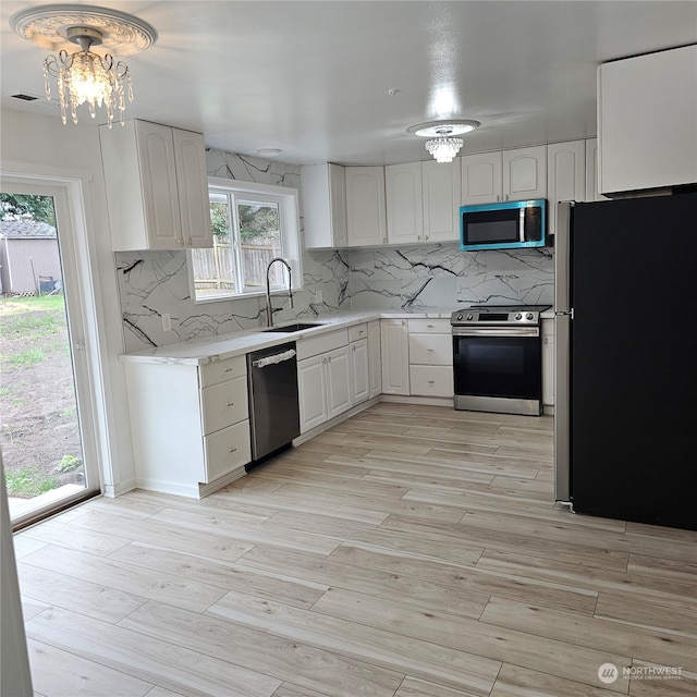 kitchen with white cabinetry, light hardwood / wood-style flooring, stainless steel appliances, and a notable chandelier