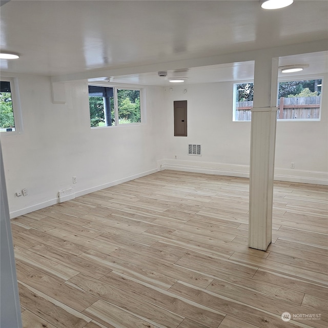 basement featuring light wood-type flooring, electric panel, and a healthy amount of sunlight