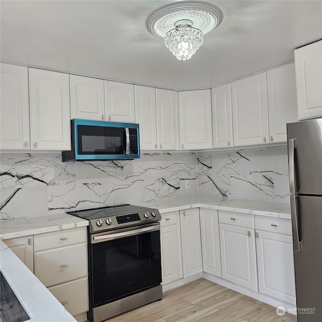 kitchen with light wood-type flooring, light stone counters, appliances with stainless steel finishes, and white cabinets