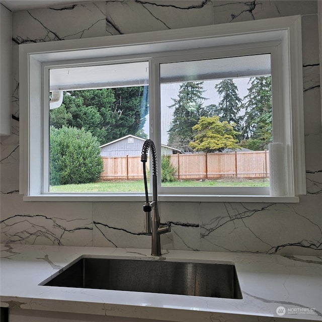 kitchen featuring plenty of natural light, light stone counters, and sink