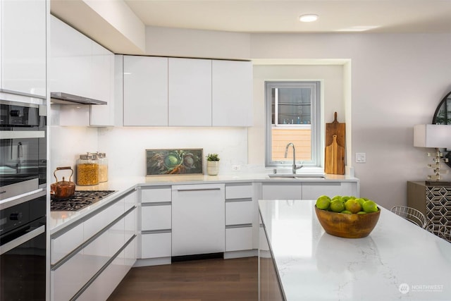 kitchen with dark wood-style flooring, light countertops, white cabinetry, stainless steel gas cooktop, and a sink