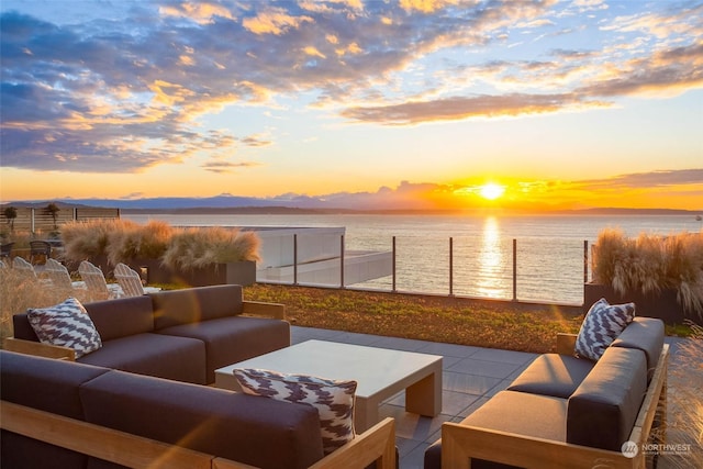 patio terrace at dusk with a water view, fence, and outdoor lounge area