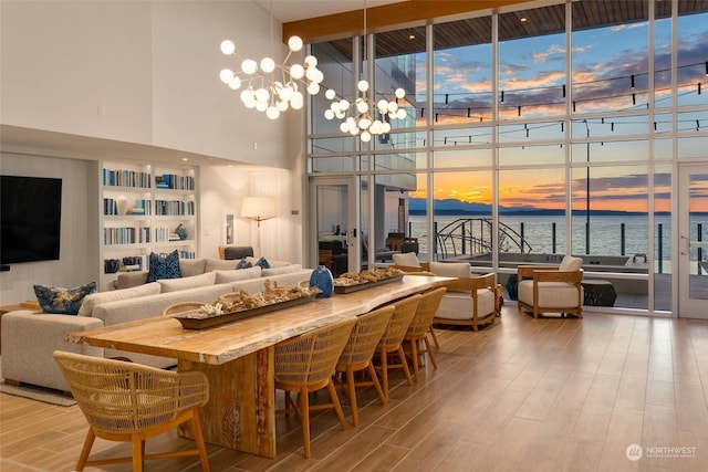 dining space featuring a water view, an inviting chandelier, light wood-style floors, expansive windows, and plenty of natural light