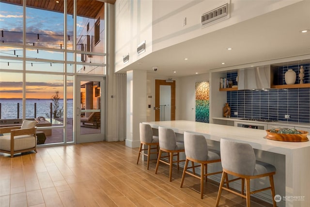 kitchen with a breakfast bar area, a water view, visible vents, light countertops, and wall chimney range hood