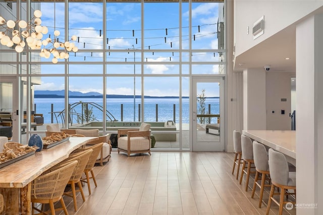 dining room featuring a water and mountain view, expansive windows, a healthy amount of sunlight, light wood-style floors, and a notable chandelier