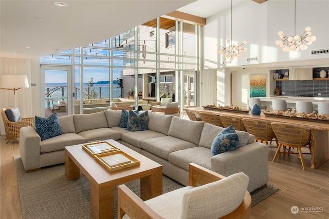 living room featuring a notable chandelier, a water view, visible vents, light wood-style floors, and a wall of windows