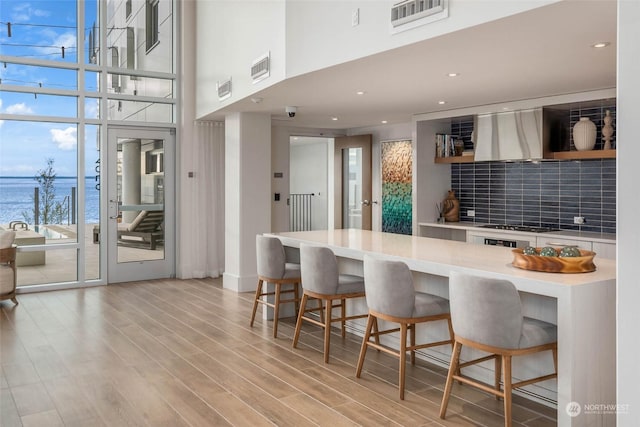 kitchen with light countertops, wall chimney range hood, a kitchen bar, and open shelves