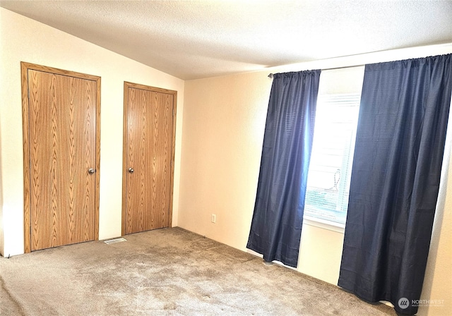 unfurnished bedroom featuring a textured ceiling, vaulted ceiling, and light colored carpet