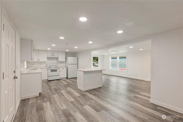 kitchen featuring recessed lighting, white appliances, a sink, light countertops, and light wood finished floors