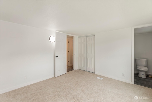 unfurnished bedroom featuring carpet floors, ensuite bath, baseboards, and a closet