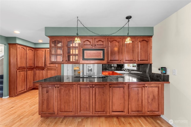 kitchen with hanging light fixtures, kitchen peninsula, stainless steel refrigerator with ice dispenser, and light hardwood / wood-style floors