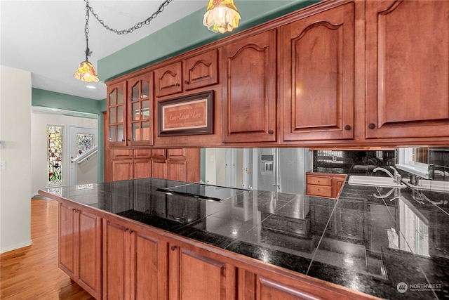 kitchen with tasteful backsplash, hanging light fixtures, kitchen peninsula, black electric stovetop, and light wood-type flooring