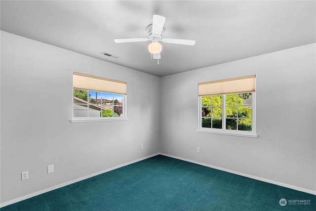 unfurnished room featuring dark colored carpet, a wealth of natural light, and ceiling fan