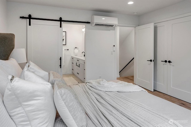 bedroom featuring a barn door, connected bathroom, light wood-style flooring, a wall mounted AC, and recessed lighting