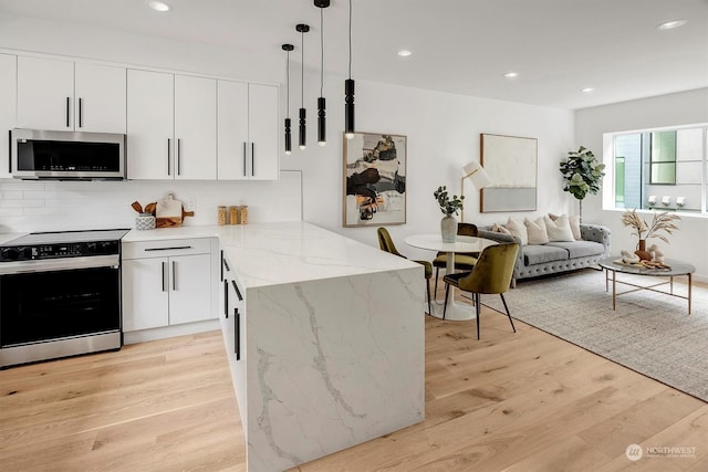 kitchen featuring a peninsula, range with electric stovetop, light wood-type flooring, tasteful backsplash, and stainless steel microwave