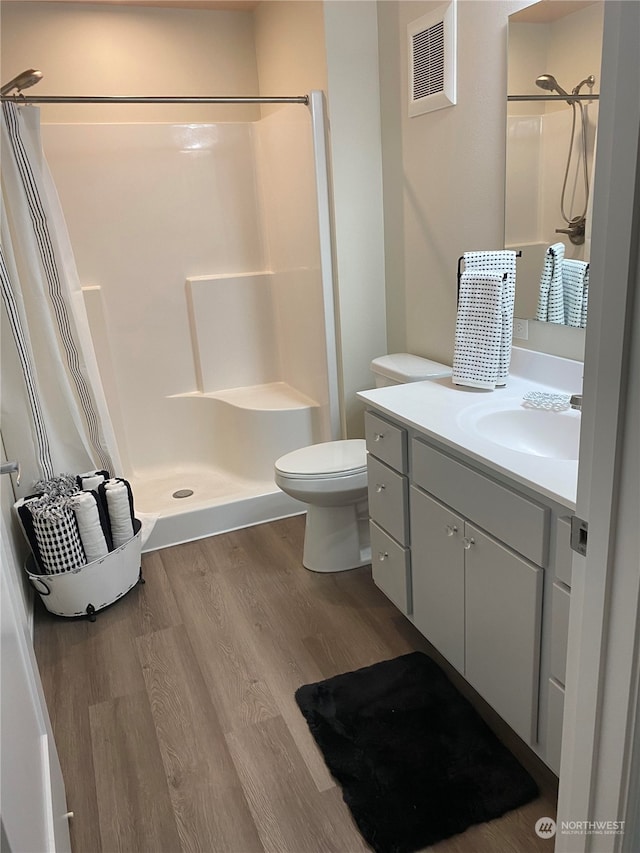 bathroom featuring wood-type flooring, vanity, toilet, and walk in shower