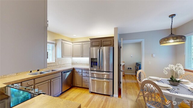 kitchen with sink, stainless steel appliances, tasteful backsplash, light hardwood / wood-style flooring, and decorative light fixtures