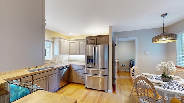 kitchen with tasteful backsplash, decorative light fixtures, stainless steel appliances, light wood-type flooring, and a sink