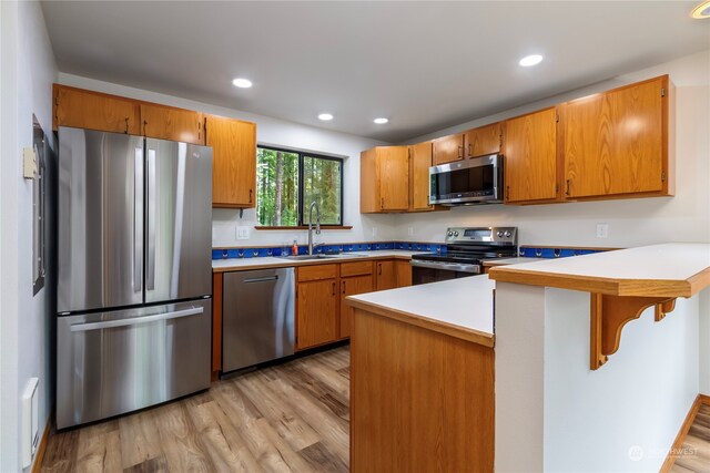 kitchen featuring a kitchen breakfast bar, kitchen peninsula, stainless steel appliances, light hardwood / wood-style flooring, and sink