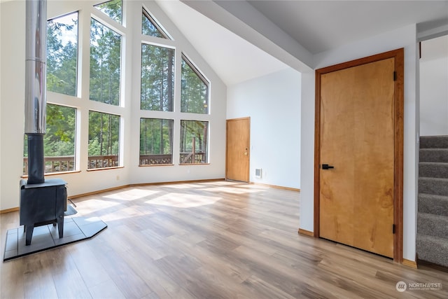 unfurnished living room with light wood-type flooring, a wood stove, and high vaulted ceiling