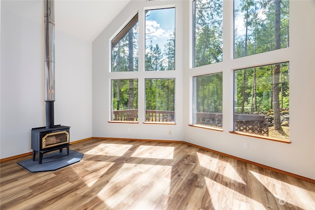 living room with a wood stove, light wood-type flooring, and high vaulted ceiling