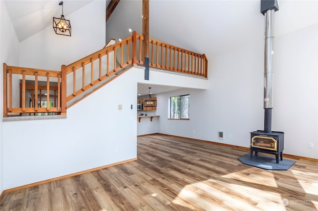 unfurnished living room with high vaulted ceiling, beamed ceiling, a wood stove, wood-type flooring, and an inviting chandelier