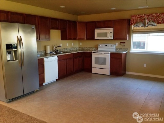 kitchen featuring light stone counters, decorative light fixtures, a sink, white appliances, and baseboards