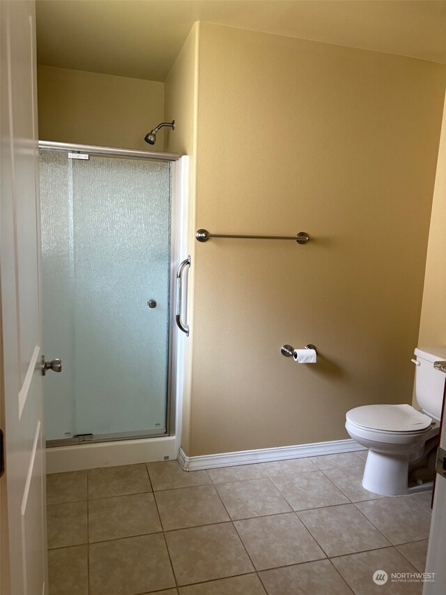 bathroom featuring toilet, a stall shower, baseboards, and tile patterned floors