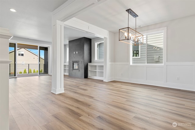 unfurnished living room with a fireplace, a notable chandelier, ornate columns, and light wood-type flooring