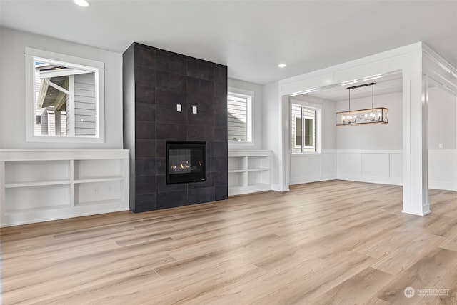 unfurnished living room featuring built in shelves, light hardwood / wood-style floors, and a tile fireplace