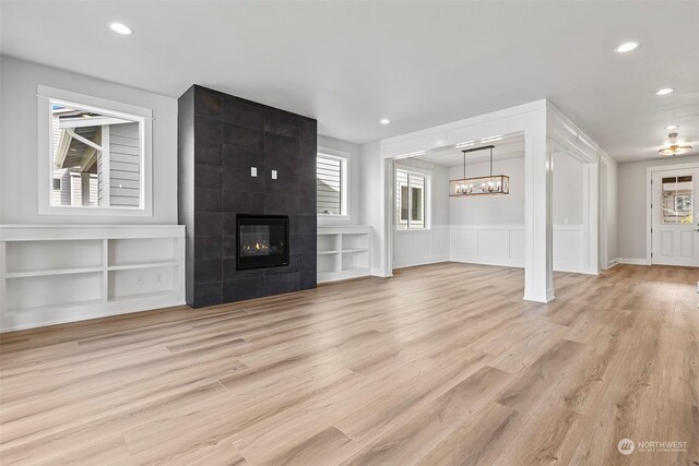 unfurnished living room with light wood-type flooring, a tiled fireplace, and built in shelves