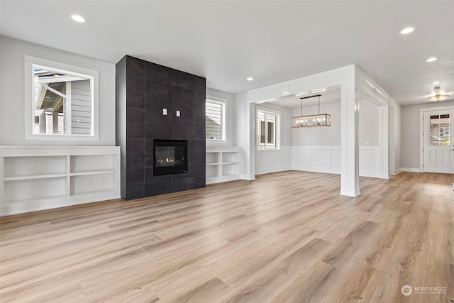 unfurnished living room with light wood-style floors, a wealth of natural light, and a tiled fireplace