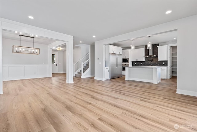 unfurnished living room with light wood-style floors, recessed lighting, a wainscoted wall, and stairs